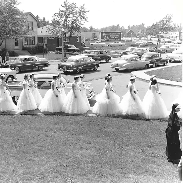 photo of 1958 graduates of MSM walking across the lawn in their white dresses