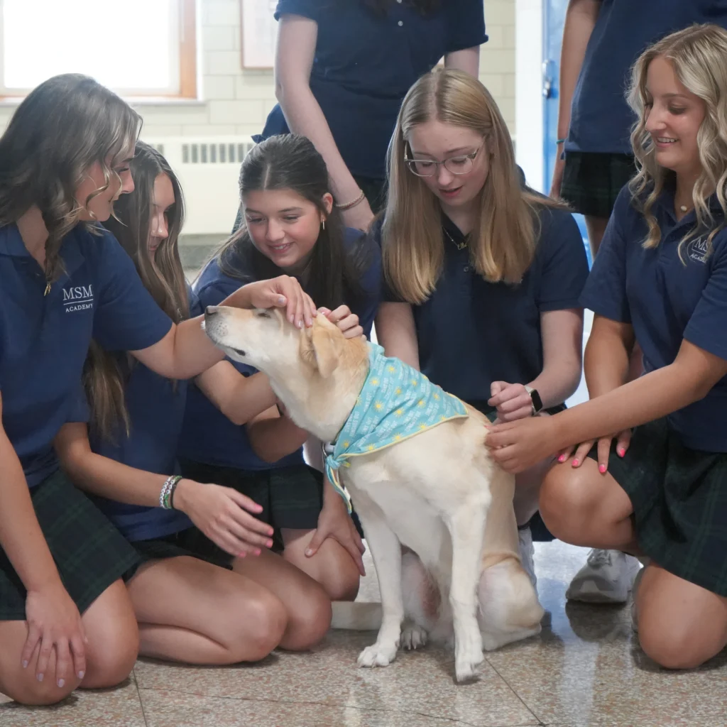 students in uniform sitting on the floor petting therapy dog, Trixie