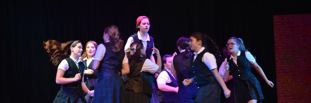 A group of girls singing and performing in the school musical