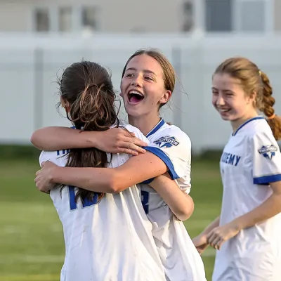 girls in soccer uniform smiling and hugging after a big score