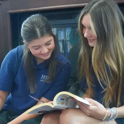 two girls in uniform smiling and looking at a workbook