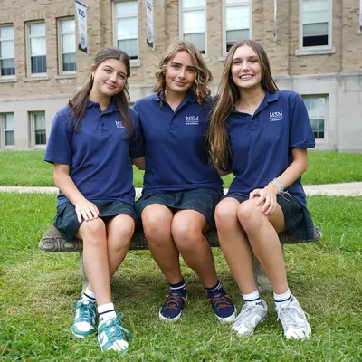 Three girls in uniform sitting on a bench in front of MSM